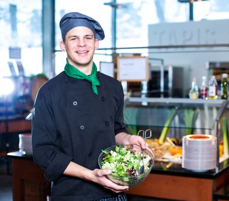 Un apprenti spécialiste en système de restauration tient un saladier rempli de salade