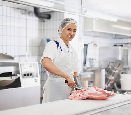 Un apprenti assistant en boucherie et charcuterie découpe une pièce de viande