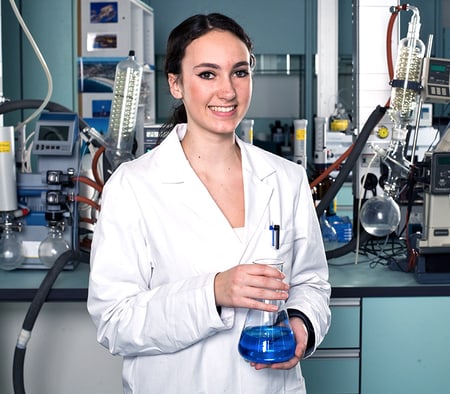 Une apprentie laborantine en chimie tient une solution bleue dans un verre
