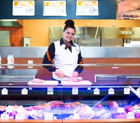 Lernende Fleischfachfrau (Feinkost und Veredelung) schneidet ein Fleisch hinter der Ladentheke