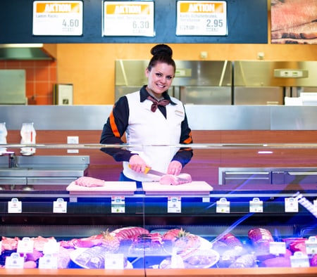 Une apprentie bouchère-charcutière (Commercialisation) découpe de la viande derrière le comptoir