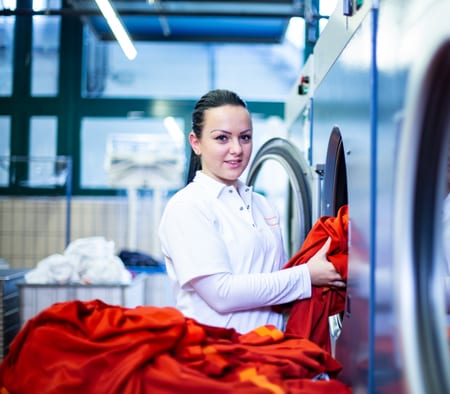 Lernende Fachfrau Textilpflege lägt Wäsche in die Waschmaschine