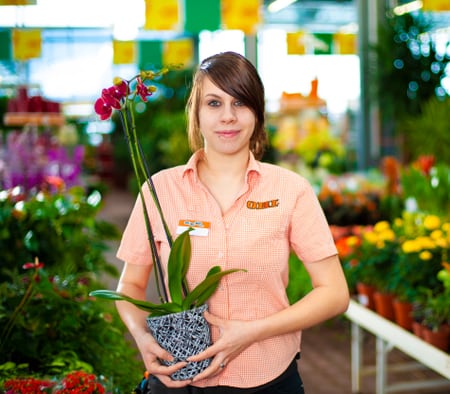 Une apprentie gestionnaire du commerce de détail (Garden) tient une orchidée en pot