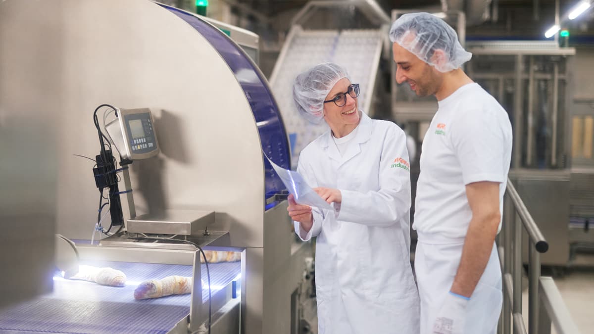 Vorgesetzte unterhält sich vor Produktionsanlage mit Mitarbeitendem