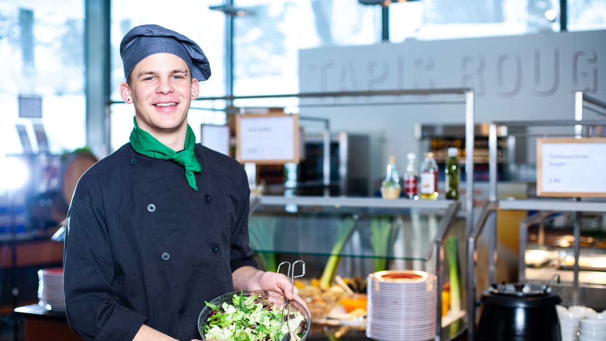 Lernender Systemgastronomiefachmann hält eine Schüssel voller Salat