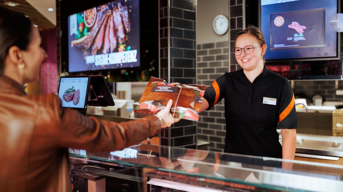 Frau übergibt Kundin an Theke Fleischprodukt