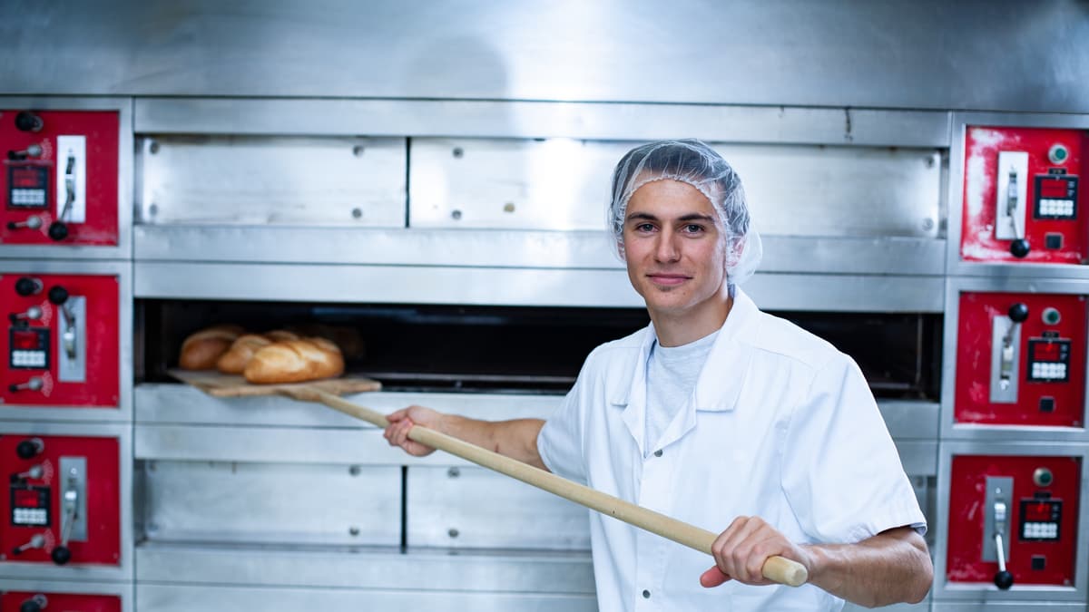 Lerndner Bäcker/Konditor/Confiseur schiebt Brot in den Ofen