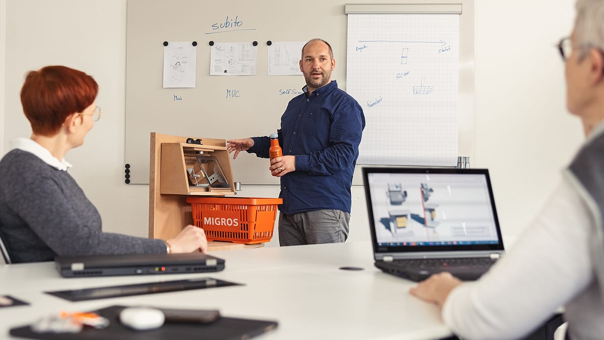 Drei Personen mit Prototyp eines Self Check-Out Systems in Sitzungszimmer