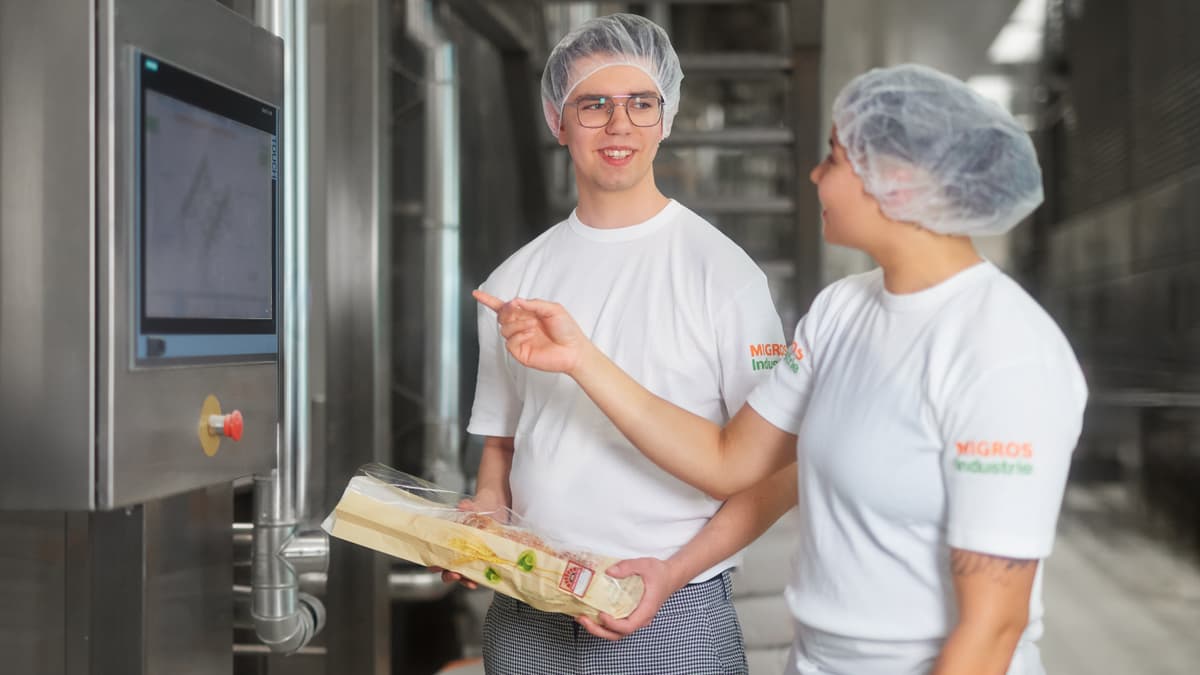 Zwei Personen stehen mit Brot vor Produktionsanlage und sprechen miteinander