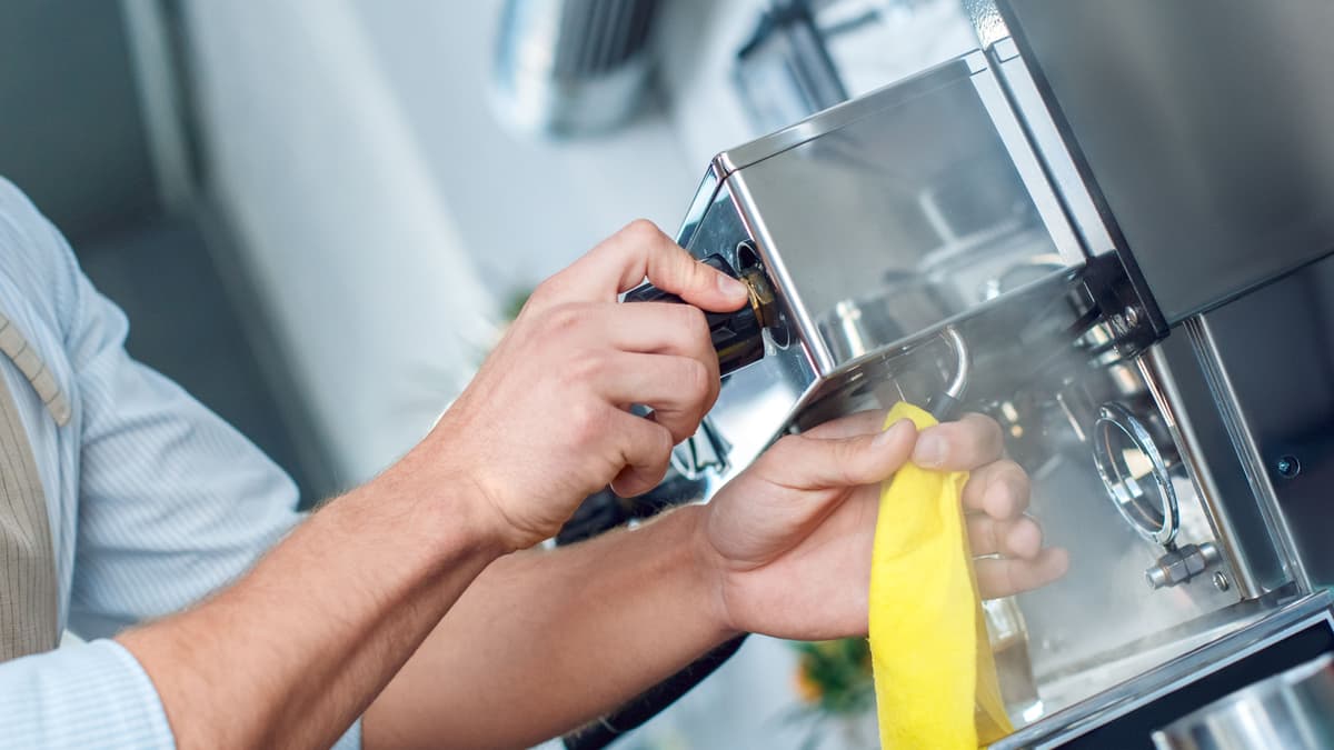 Person reinigt mit gelbem Lappen Kaffeemaschine