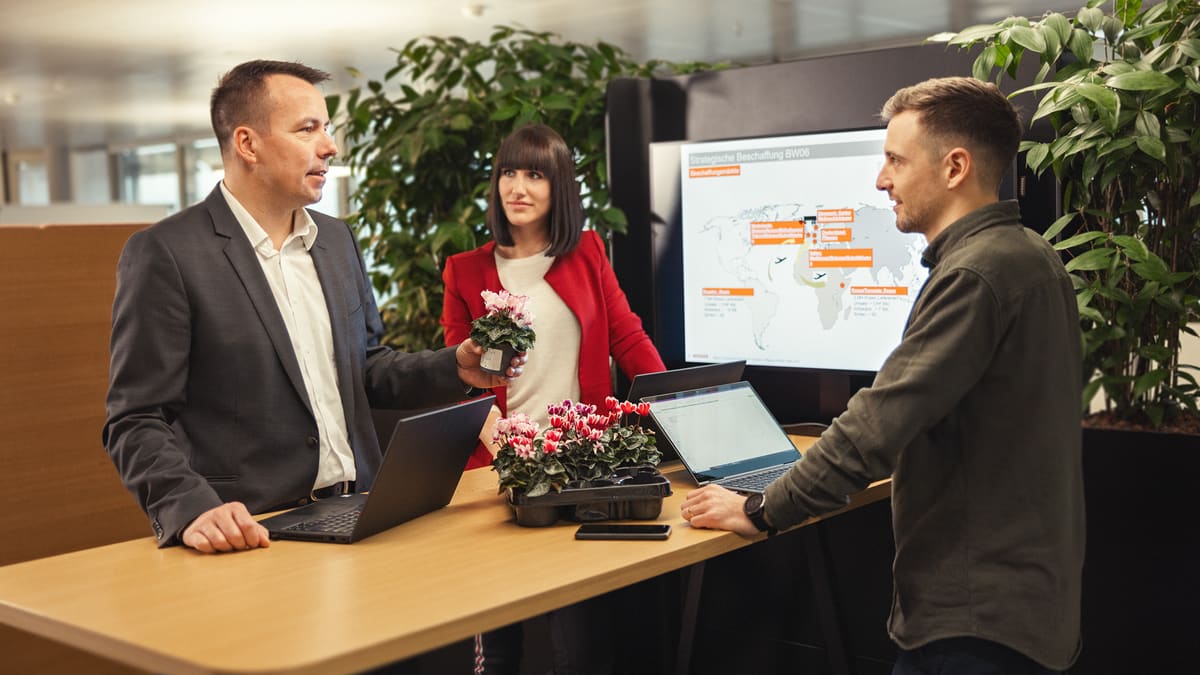 Drei Personen bei Verhandlung mit Blumen an Stehpult