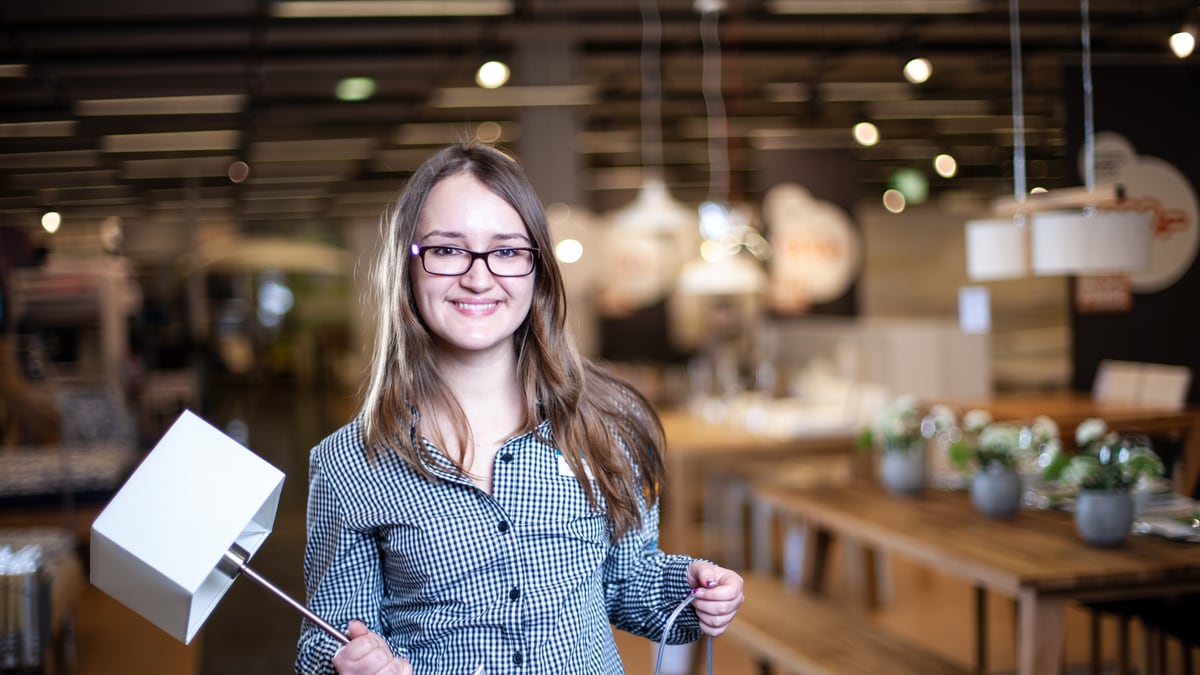 Une apprentie gestionnaire du commerce de détail (Ameublement) tient une lampe de table