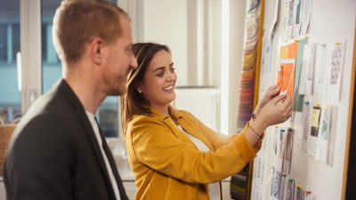 Frau und Mann betrachten Farbmuster an einer Pinwand