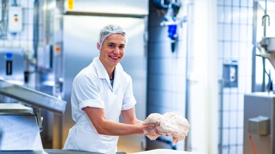 Un apprenti boucher-charcutier (Transformation) dépose un mélange de viande dans une bassine