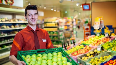 Un apprendista impiegato del commercio al dettaglio (Alimenti e generi volutturi) con una cassetta di mele