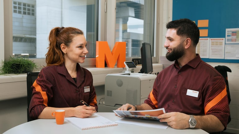 Zwei Mitarbeitende der Migros Aare in einem Gespräch im Büro einer Filiale