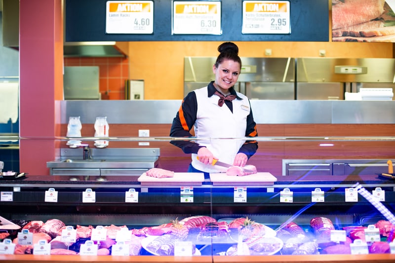 Un'apprendista macellaia-salumiera (Commercializzazione) taglia un pezzo di carne dietro il bancone