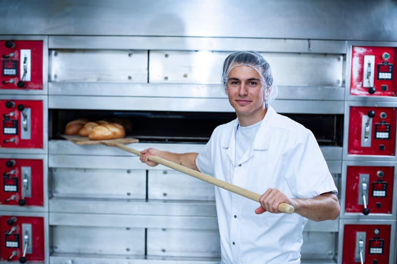 Un apprendista panettiere/confettiere/pasticciere infila il pane nel forno