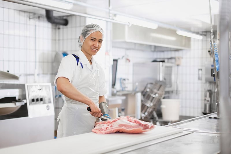 Un apprendista addetto di macelleria taglia un pezzo di carne