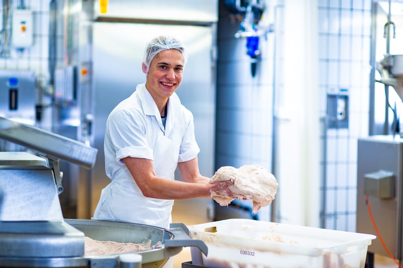 Un apprendista macellaio-salumiere (Trasformazione) sistema un pezzo di carne in un recipiente