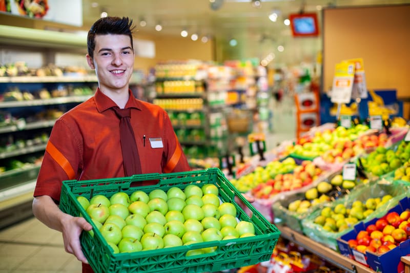Un apprendista impiegato del commercio al dettaglio (Alimenti e generi volutturi) con una cassetta di mele