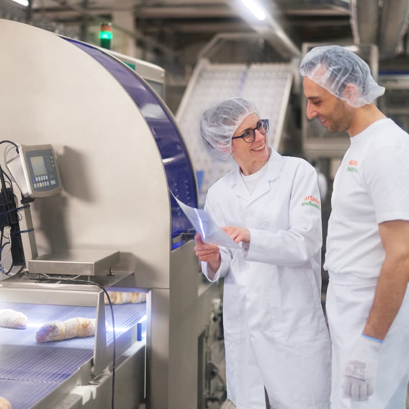 Vorgesetzte unterhält sich vor Produktionsanlage mit Mitarbeitendem