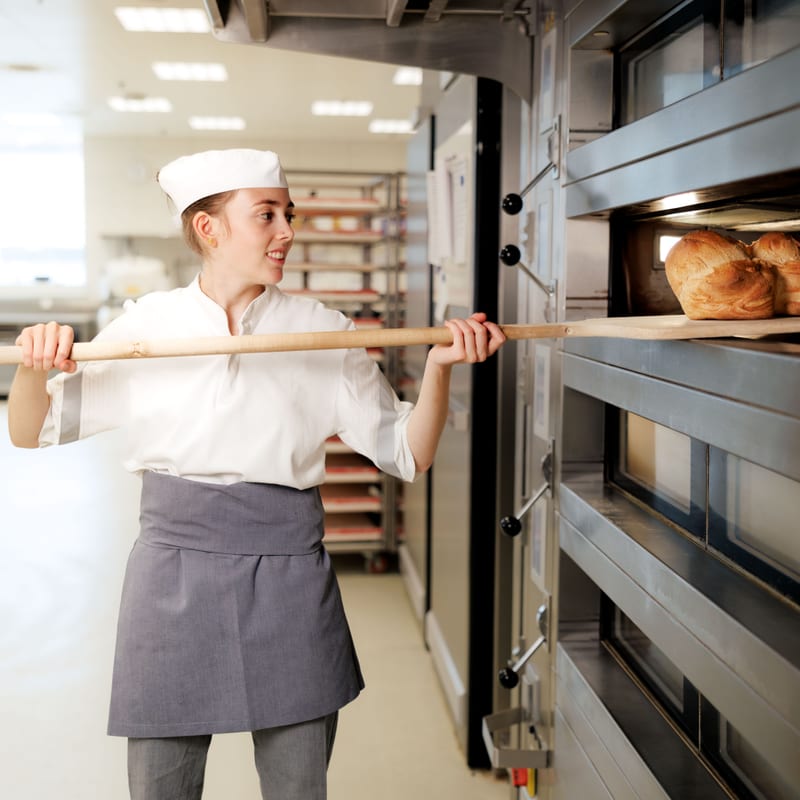 Frau nimmt Brot aus Ofen