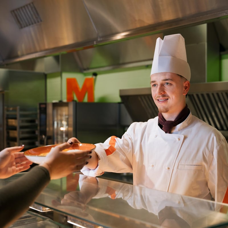 Ein Koch eines Migros Restaurants gibt einer Kundin ihr Essen aus