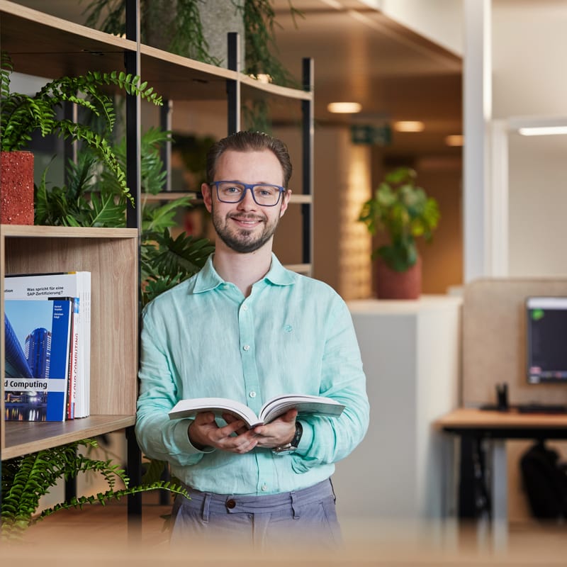 Mann steht im Büro und hält ein Buch in der Hand