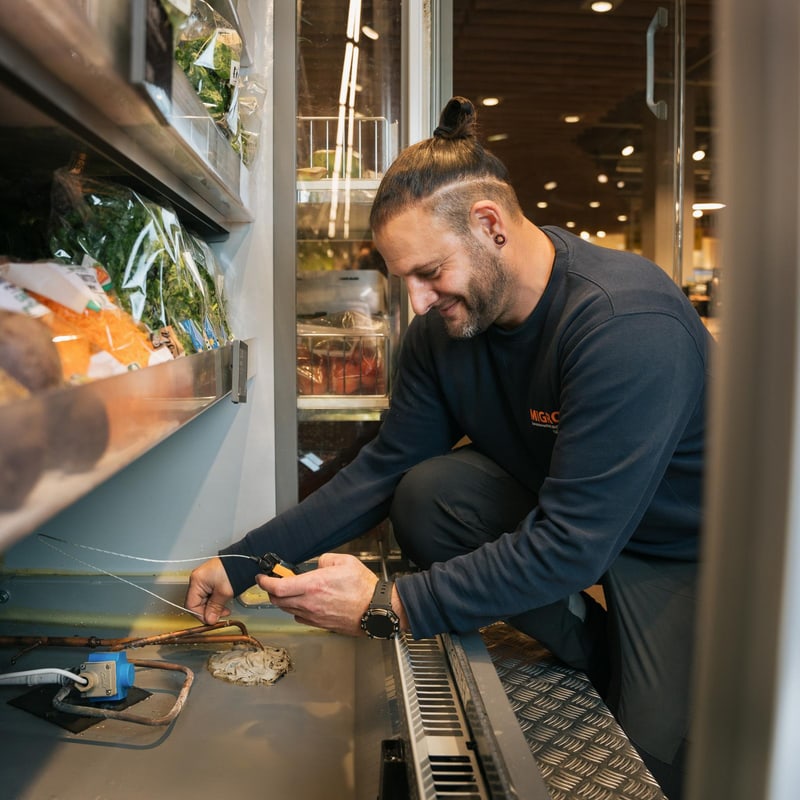 Ein Fachmitarbeiter Kältetechnik arbeitet an einem Kühlregal in der Migros Filiale