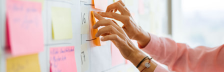 Mitarbeitende klebt Post It Zettel an die Wand